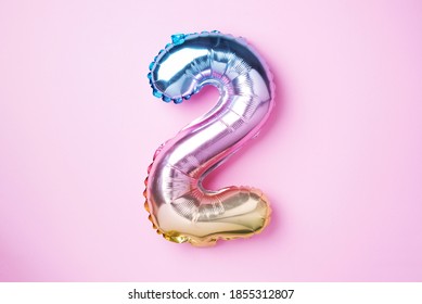 Creative layout. Rainbow foil balloon number and digit two 2. Birthday greeting card. Anniversary concept. Top view. Copy space. Stylish colored numeral over pink background. Numerical digit