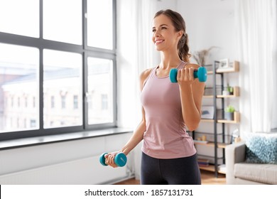fitness, sport en gezonde levensstijl concept - lachende jonge vrouw met halters thuis oefenen