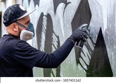 Artista de graffiti en acción, dibujando en la pared con pintura en aerosol en una lata, usando mascarilla protectora / respirador con filtros. Concepto de cultura de arte callejero.