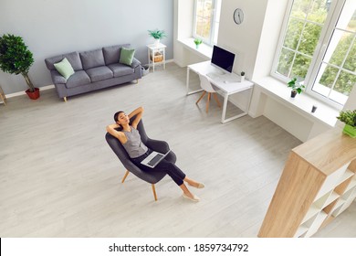 Amplia sala de estar, estudio o espacio de trabajo de oficina con una mujer tomando un descanso del trabajo en una laptop. Interior moderno de apartamento nuevo con grandes ventanales y persona relajándose en un cómodo sillón. Angulo alto