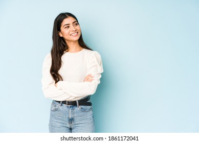 Young indian woman isolated on blue background smiling confident with crossed arms.