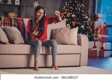 Foto de una mujer joven hermosa atractiva loca emocionada sonriente positiva sentada en el sofá jugando a un videojuego gritando sí en casa