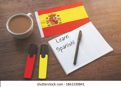 spanische Nationalflagge, Tasse Kaffee, Notizbuch mit der Aufschrift Spanisch lernen, zwei Markierungen auf dem Desktop, Fremdsprachenlernkonzept