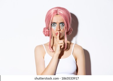 Close-up of angry girl with pink wig, frowning and shushing with mad face, standing over white background