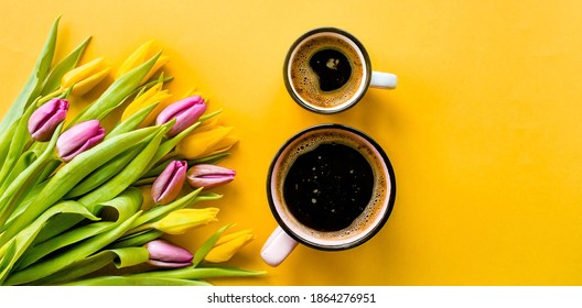 Banner.Two cups of hot, morning coffee in the shape of the number 8 and a bouquet of yellow-lilac tulips on a bright yellow background. View from above.Copy space for text. The concept of holidays.
