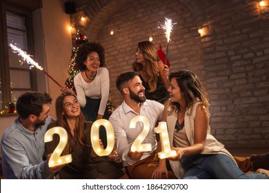 新年のパーティーで楽しんでいる若い友人のグループは、次の新年を表す照明番号2021を保持し、真夜中のカウントダウンで線香花火で手を振っています