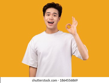 Estoy bien. Retrato de un asiático feliz y emocionado haciendo un gesto de aprobación con los dedos, sonriendo, mostrando que está bien, aislado sobre el fondo naranja del estudio. Adolescente seguro de sí mismo es genial