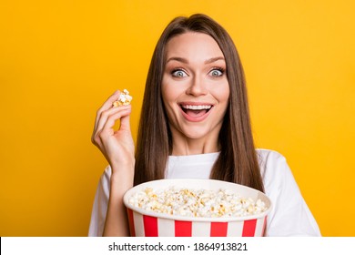 Photo portrait of funny excited smiling girl keeping pop corn carton box watching adventurous film isolated vivid yellow color background