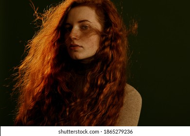 Beautiful redhead woman with natural long curly hair posing on dark olive green background. Hair care, beauty conception. Copy, empty space for text