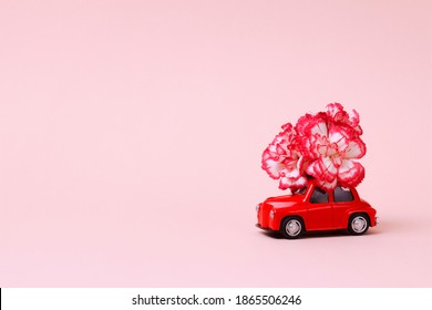 Día Mundial de la Mujer. Pequeño coche de juguete retro rojo con una flor roja y blanca en el techo sobre un fondo rosa. Entrega de regalos para el día de los enamorados. Copie el espacio.
