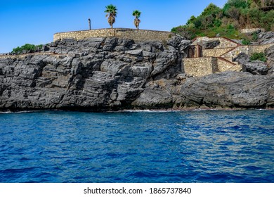 Vista desde el mar al parque abandonado Emirgan Ulas Mesire Yeri en Alanya (Turquía). Dos palmeras crecen en una terraza artificial de piedra en una roca de granito entre aguas turquesas