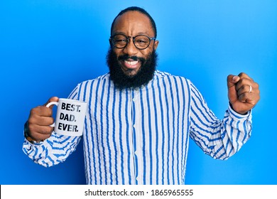 若いアフリカ系アメリカ人男性がコーヒーのマグカップを飲み、これまでで最高のお父さんのメッセージを誇らしげに叫び、勝利と成功を祝い、腕を上げて非常に興奮