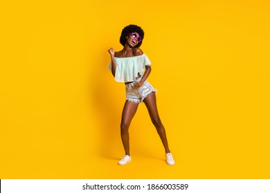 Foto van de volledige lengte van het lichaam van een vrouw met een zwarte huid die in het weekend danst en een stervormige zonnebril draagt, geïsoleerd op een levendige gele achtergrond