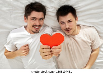 Happy couple of young gay men hide hold red paper heart lying on back on valentine's day in blur
