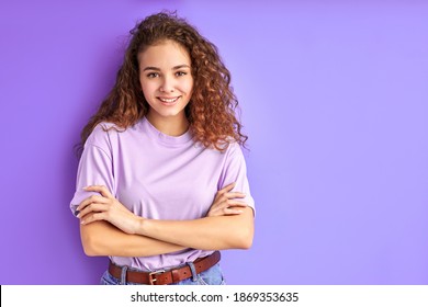 カメラ目線のカジュアルな t シャツで魅力的な女性、組んだ腕でポーズをとって恥ずかしがり屋の白人巻き毛ティーンエイ ジャーの女の子の肖像画。紫色のスタジオの背景