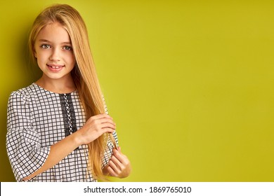 Cô bé đang chạm vào mái tóc vàng dài của mình, thích có một mái tóc hoàn hảo, nhìn vào máy ảnh bị cô lập trên nền xanh