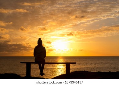 Toma de gran angular de la silueta de una mujer sentada en un banco mirando la tranquila puesta de sol sobre el océano
