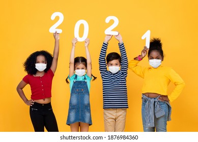 黄色の背景に隔離された2021年の数字を持つ医療用フェイスマスクを着用したかわいい混血の子供たち、パンデミックの概念の時代の新年