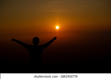 silhouette of joyful boy playing with sun in the golden orange background. Dawn in mountain area. Hand spread boy joyful to see sun rise in early morning