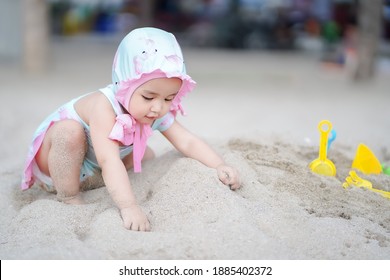Asian cute baby girl in swimsuit playing on the sand beach on sunny day
