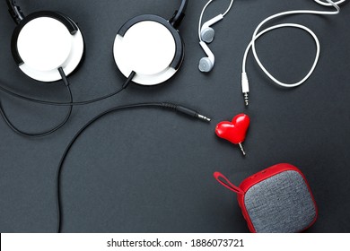 Un divisor de auriculares en forma de corazón para una pareja enamorada. Conectado a un altavoz portátil rojo y dos pares de auriculares: plano. Día de San Valentín, amor, tecnología moderna, espacio de copia, fondo negro.