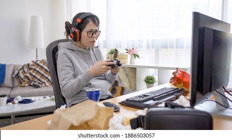 夏休みに自宅で怒った顔でジョイスティックでビデオゲームをプレイするヘッドセットを着たネガティブなアジアの韓国人ゲーマー女性。