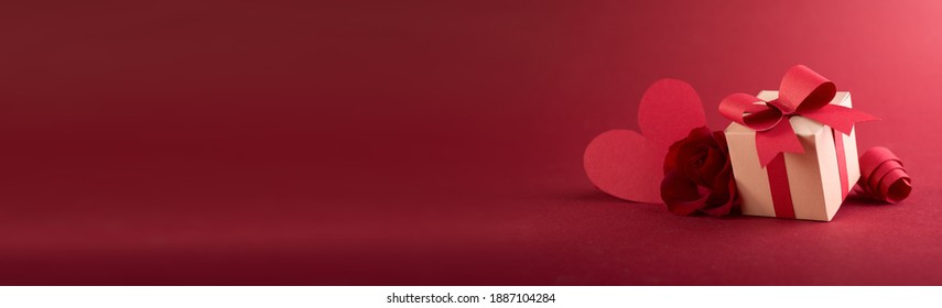 Paper art Valentine's day concept banner with hand made gift box, paper cut ribbon, bow, and a lot of hearts on a red background with space for text.