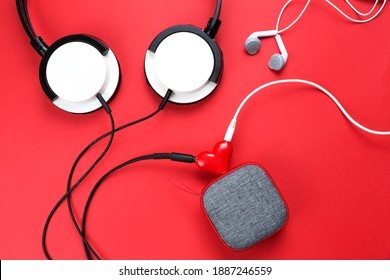 Un divisor de auriculares en forma de corazón para una pareja enamorada. Conectado a un altavoz portátil rojo y dos pares de auriculares: plano. día de san valentín, amor, tecnología moderna, espacio de copia