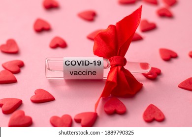 분홍색 배경에 빨간색 하트 옆에 발렌타인 데이 선물로 COVID-19 백신이 담긴 앰플