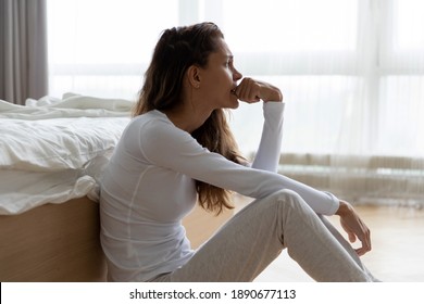 Wanita yang tidak bahagia memikirkan masalah, duduk di lantai di kamar tidur sendirian, wanita muda yang frustrasi menggigit kuku, merasa kesepian dan sedih, menderita hubungan yang buruk, putus atau bercerai