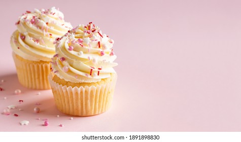 Vanille Cupcakes mat Crème Kéis frosting a rosa Sprëtz op rosaem Hannergrond. Saint Vältesdag oder Gebuertsdag Dessert. Schéin feierlech Iessen fir Hochzäit oder Puppelchen Dusch Meedchen. Plaz kopéieren.