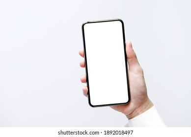 スマートフォンのモックアップ。黒い電話の白い画面を持っている手を閉じます。白い背景で隔離されました。携帯電話のフレームレス デザイン コンセプト。