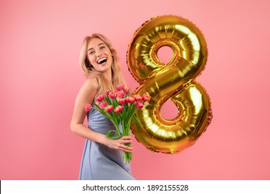 Fröhliche tausendjährige Dame mit Blumenstrauß und Ballon Nummer acht im Frühlingsurlaub über rosafarbenem Studiohintergrund. Fröhliche junge Blondine, die den Tag der Frau feiert. Festliches Konzept