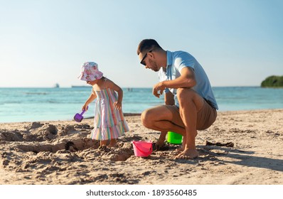 family, leisure and people concept - father and baby daughter playing with sand toys on summer beach