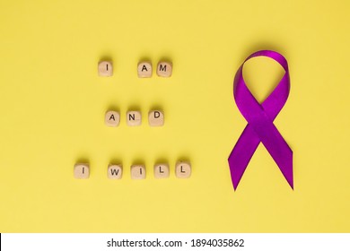 Houten kubussen met tekst van de slogan van Wereldkankerdag ik ben en ik zal en een paars lint, op een gele ondergrond. plat leggen