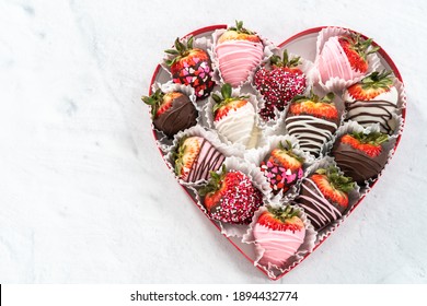 Herzförmige Schachtel mit verschiedenen Erdbeeren mit Schokoladenüberzug auf weißem Hintergrund.