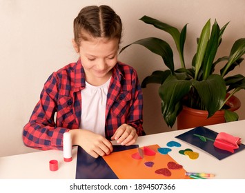 格子縞のシャツを着た子供が、家で心を込めて紙のギフトカードを作ります。子供のDIY、趣味のコンセプト、自分の手で贈る。バレンタインデー、母の日の飾り付け。