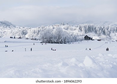 冬の活動をしている人々、雪に覆われた丘、背景の小さな村、手前の雪の吹きだまりのある冬の風景