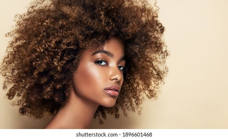 Beauty portrait of african american girl with clean healthy skin on beige background. Smiling dreamy beautiful black woman.Curly hair in afro style