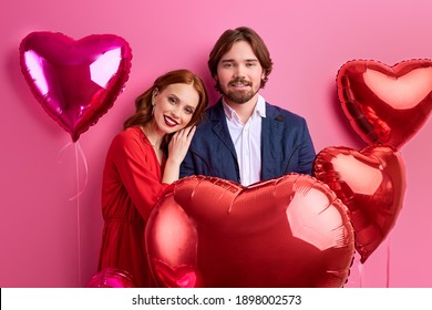 el hombre y la mujer entre los globos de aire miran la cámara aislada en el fondo rosa. Día de San Valentín, concepto de amor