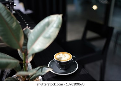 Hot Latte - Secangkir kopi dengan susu dan seni latte pola daun yang indah di atas meja kayu dengan warna gelap dan ruang fotokopi, Sempurna untuk waktu sarapan.