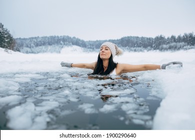 Winterzwemmen. Vrouw in bevroren meerijsgat. Zwemmers wellness in ijskoud water. Hoe te zwemmen in koud water. Mooie jonge vrouw in zen-meditatie. Grijze muts en handschoenen zwemkleding. Natuur meer