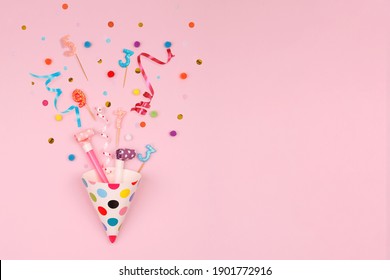 Partyhut, Konfetti und Kerzen auf rosafarbenem Hintergrund. Geburtstag, Urlaubskonzept.