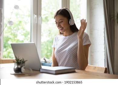 Aulas remotas. Professora jovem sorridente, tutora, iniciando uma aula distante, levantando a mão e dando boas-vindas aos alunos. Estudante interessada, sentada ao lado do computador, com fones de ouvido, iniciando o trabalho, cumprimentando o professor instrutor