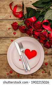 Romantischer Esstisch. Liebeskonzept für Valentinstag oder Muttertag, Hochzeitsbesteck. Blumenstrauß aus frischen Burgunder-Rosen, Vintage-Holzbretter-Hintergrund, Draufsicht