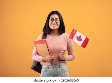 旅行、現代教育、学生交流。ノートと眼鏡をかけた若い陽気なアジアの女性、カナダの小さな旗を持つバックパック、ベージュ色の背景、スタジオ撮影、空きスペースに隔離