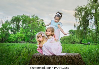 Little cute girls with butterfly wings on a large tree stump among the tall green grass. Selective focus. Blurred background.