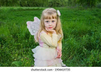 Little cute girl with butterfly wings on a large tree stump among the tall green grass. Selective focus. Blurred background.