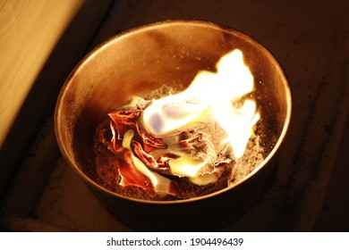 Un primer plano con enfoque selectivo del papel ardiendo dentro de un recipiente.