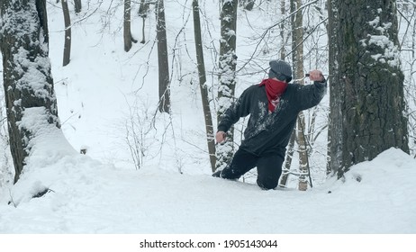 Man in red bandana and black, round glasses using two knives climbs snow covered mountain. Then he sticks the knife into tree